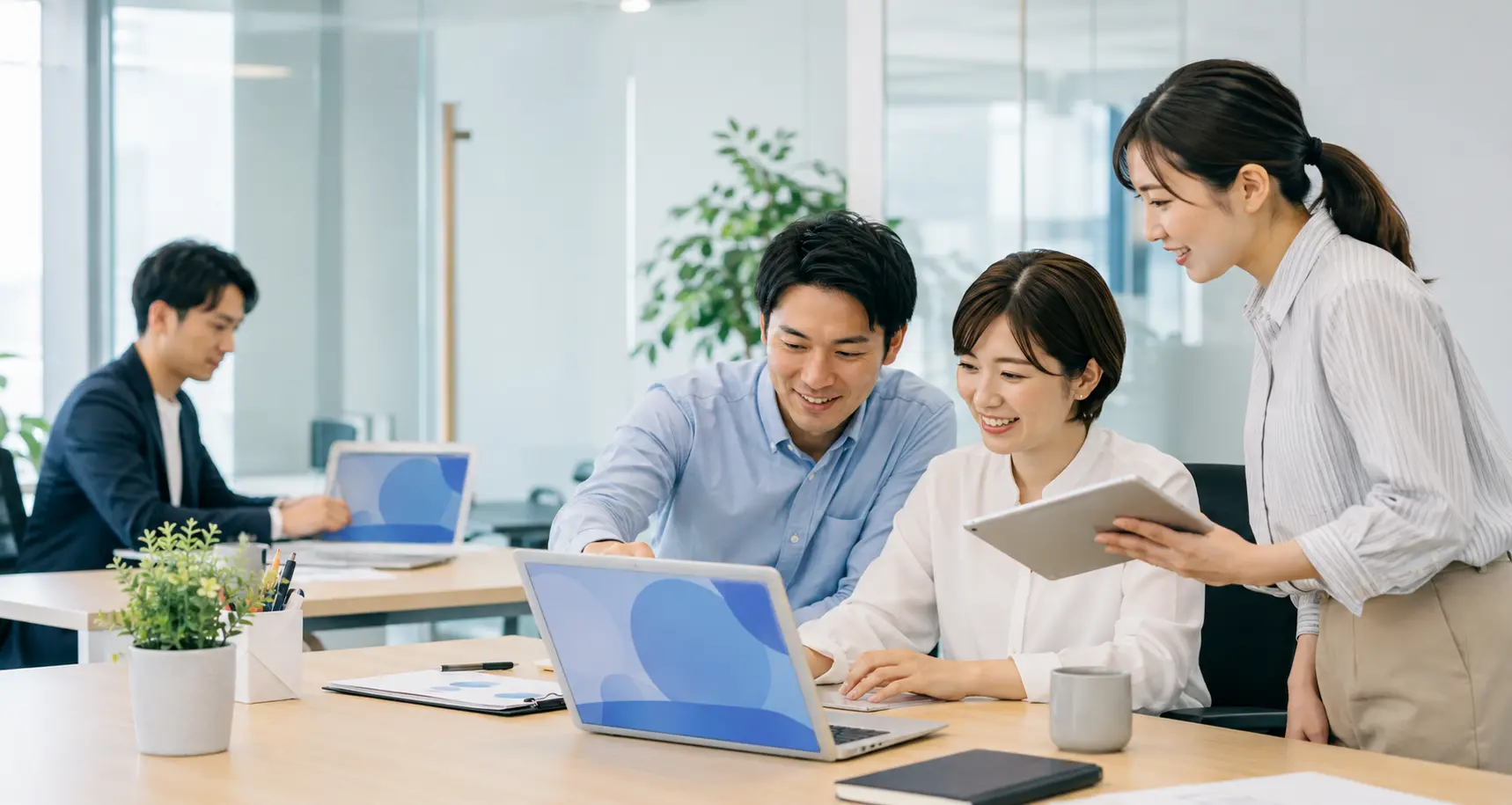 ノートパソコンとタブレットでデータを共有しながら働く人々
