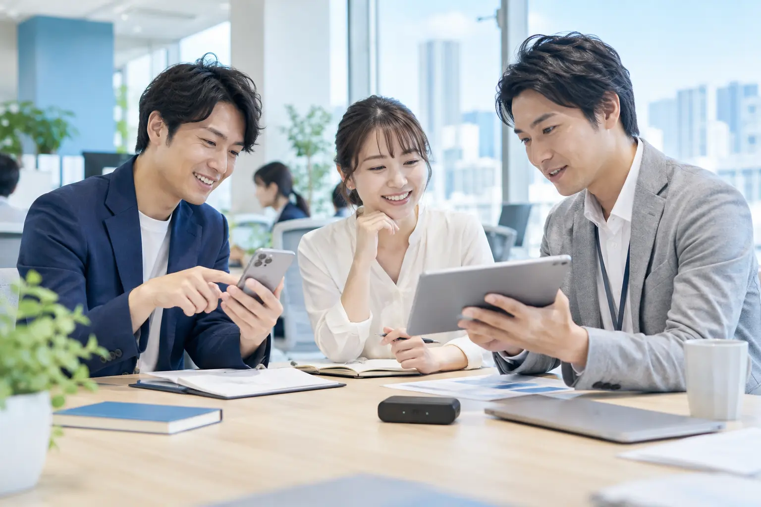 明るいオフィスでスマートフォン、タブレット、ポケットWiFiを利用する人々